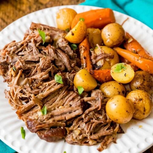 Juicy pot roast shredded on a plate beside roasted carrots and potatoes.