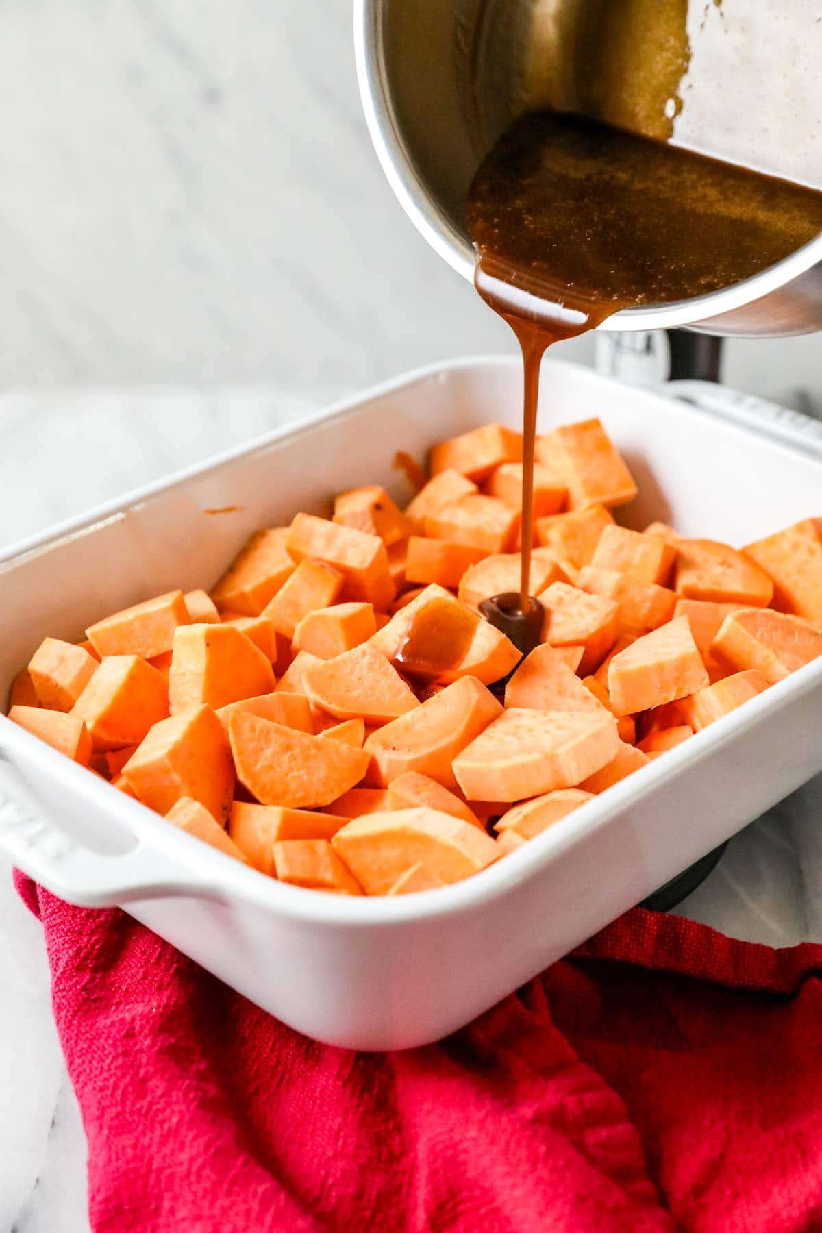 Brown sugar syrup being poured over a casserole dish of chopped sweet potatoes.