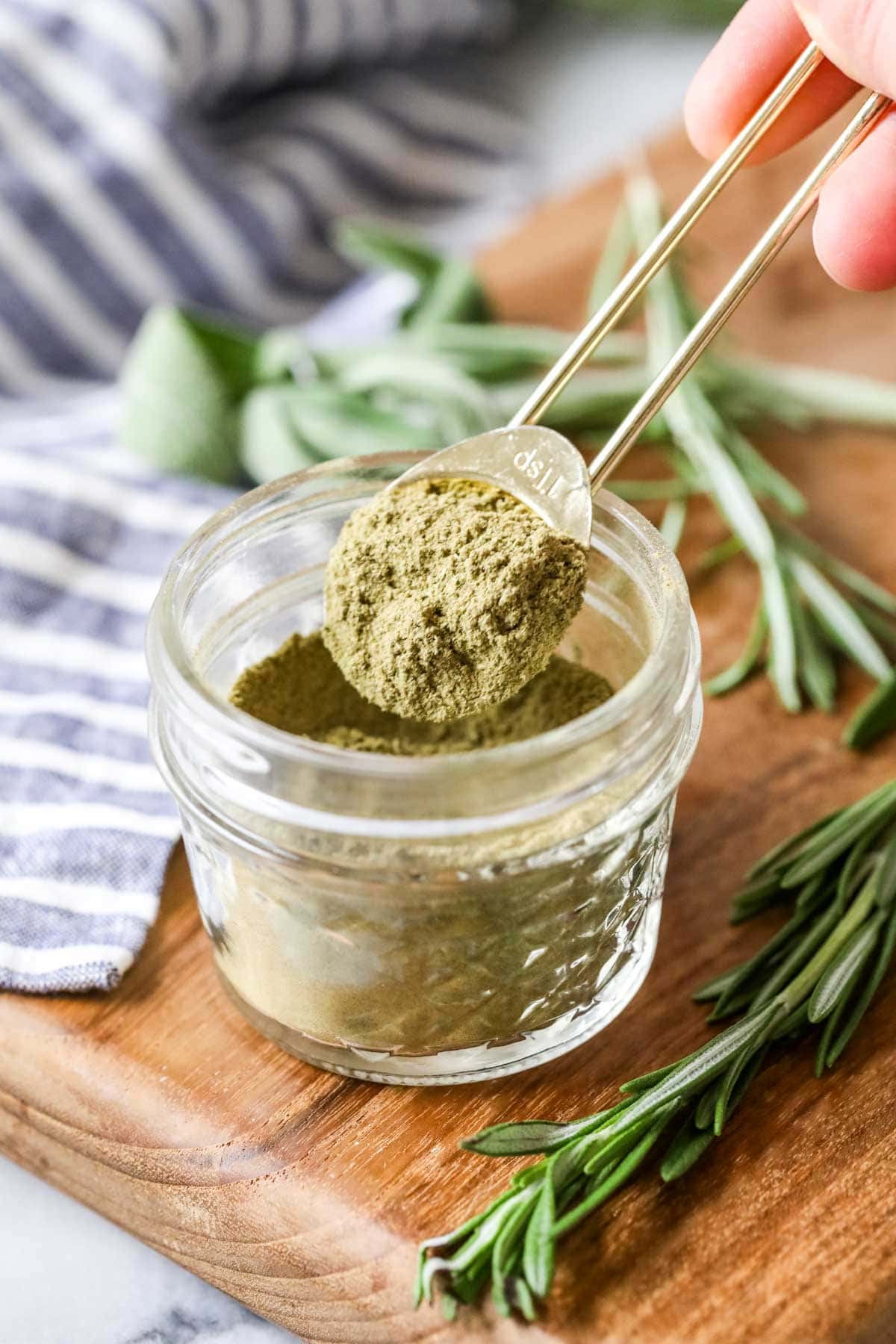 Gold measuring spoon scooping seasoning out of a small glass jar.