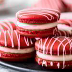 Three red velvet macarons stacked in a pyramid shape with more macarons behind.