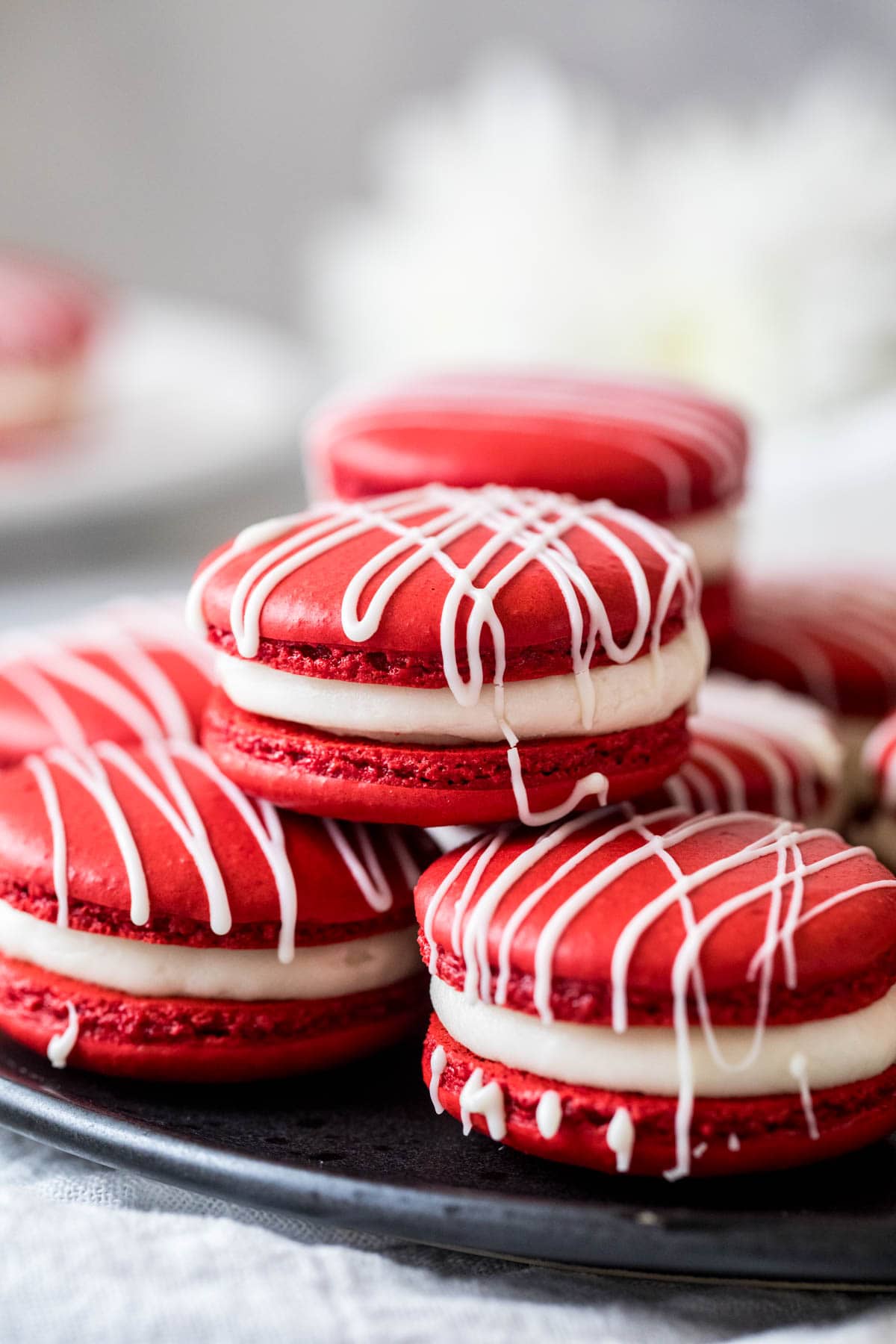 Three red velvet macarons stacked in a pyramid shape with more macarons behind.
