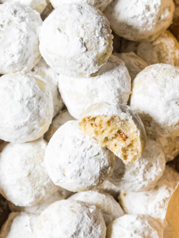 Overhead view of snowball cookies in a parchment lined bread pan with one cookie missing a bite.