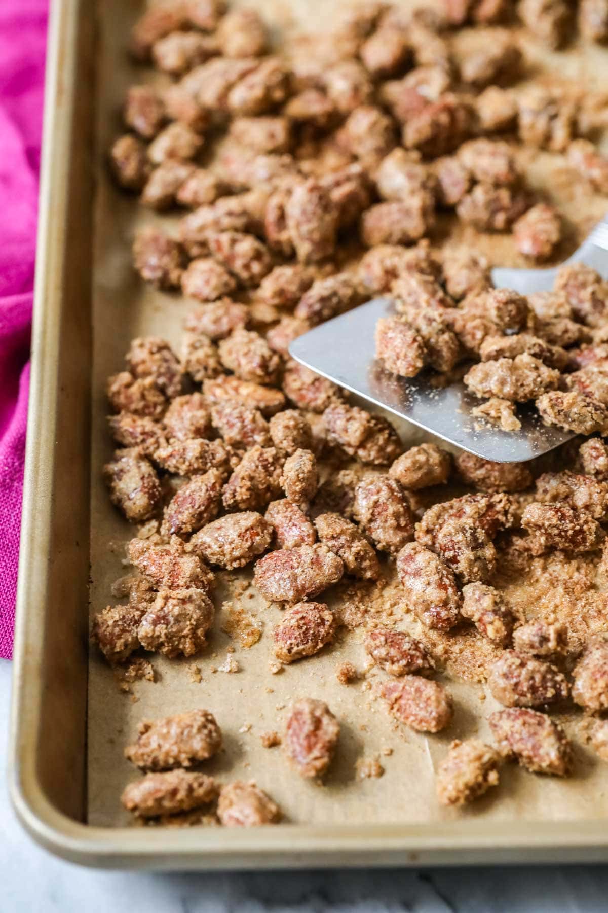 Spatula resting on a sheet pan of cinnamon sugar roasted almonds.