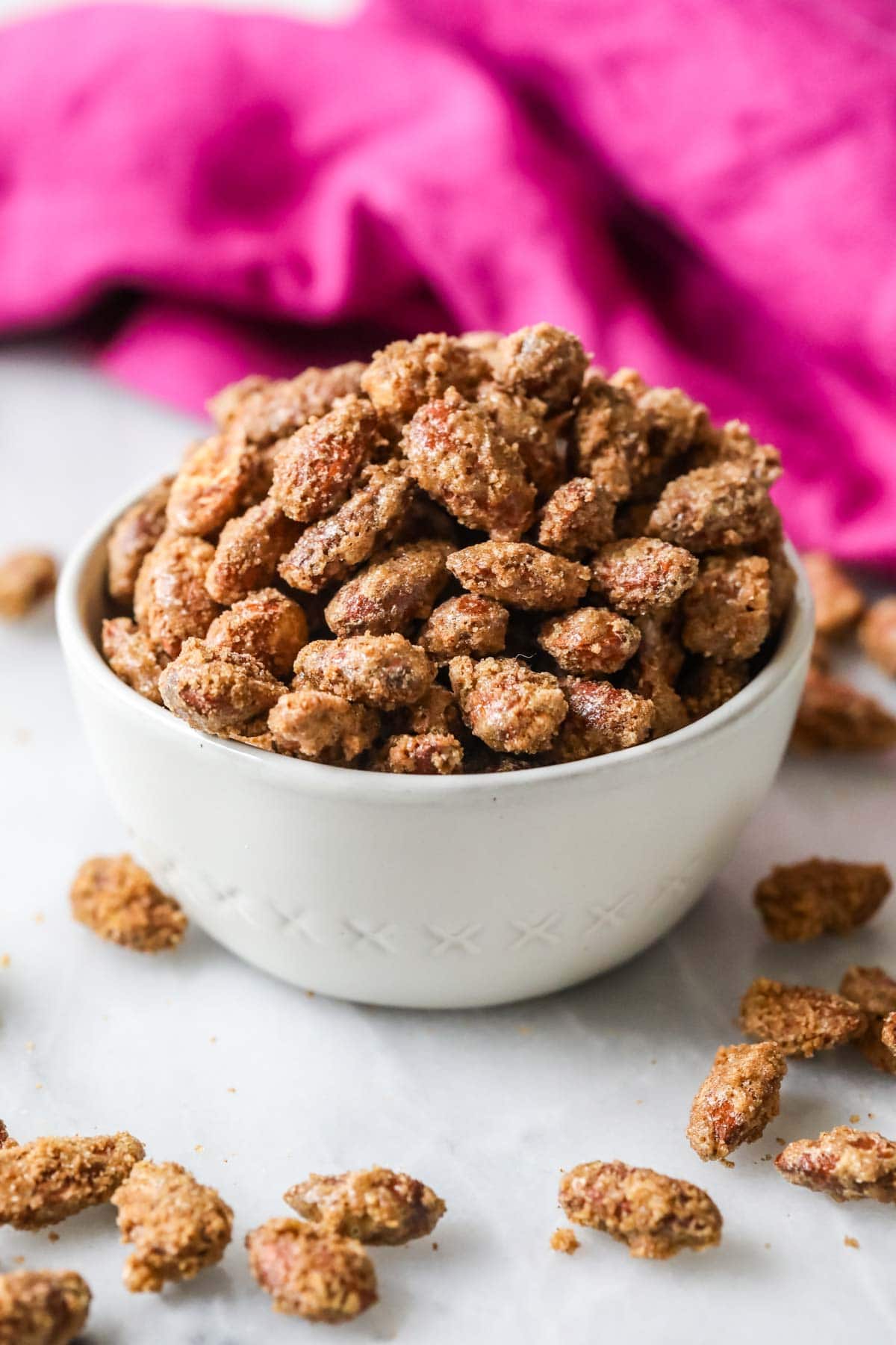 White bowl of candied almonds with a bright pink tea towel in the background.
