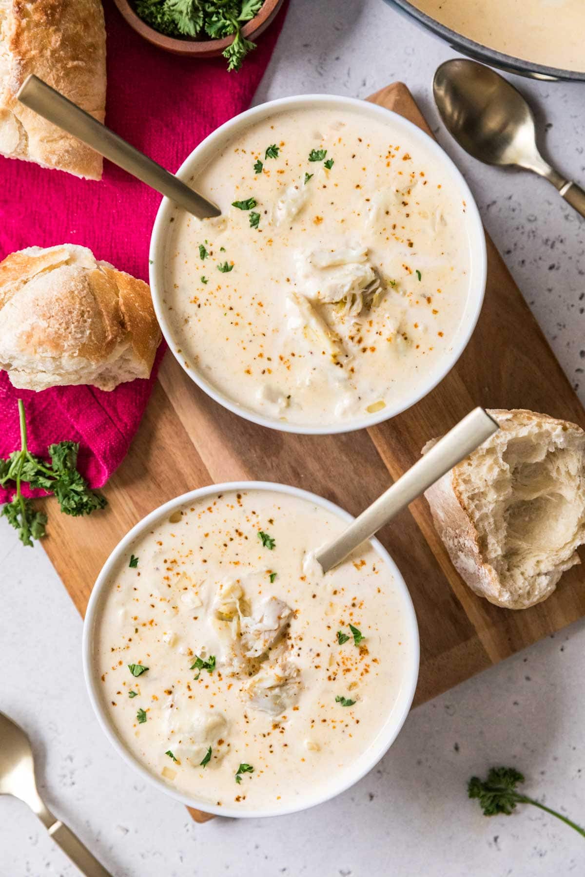 Overhead view of two bowls of cream of crab with hunks of crusty bread beside them.
