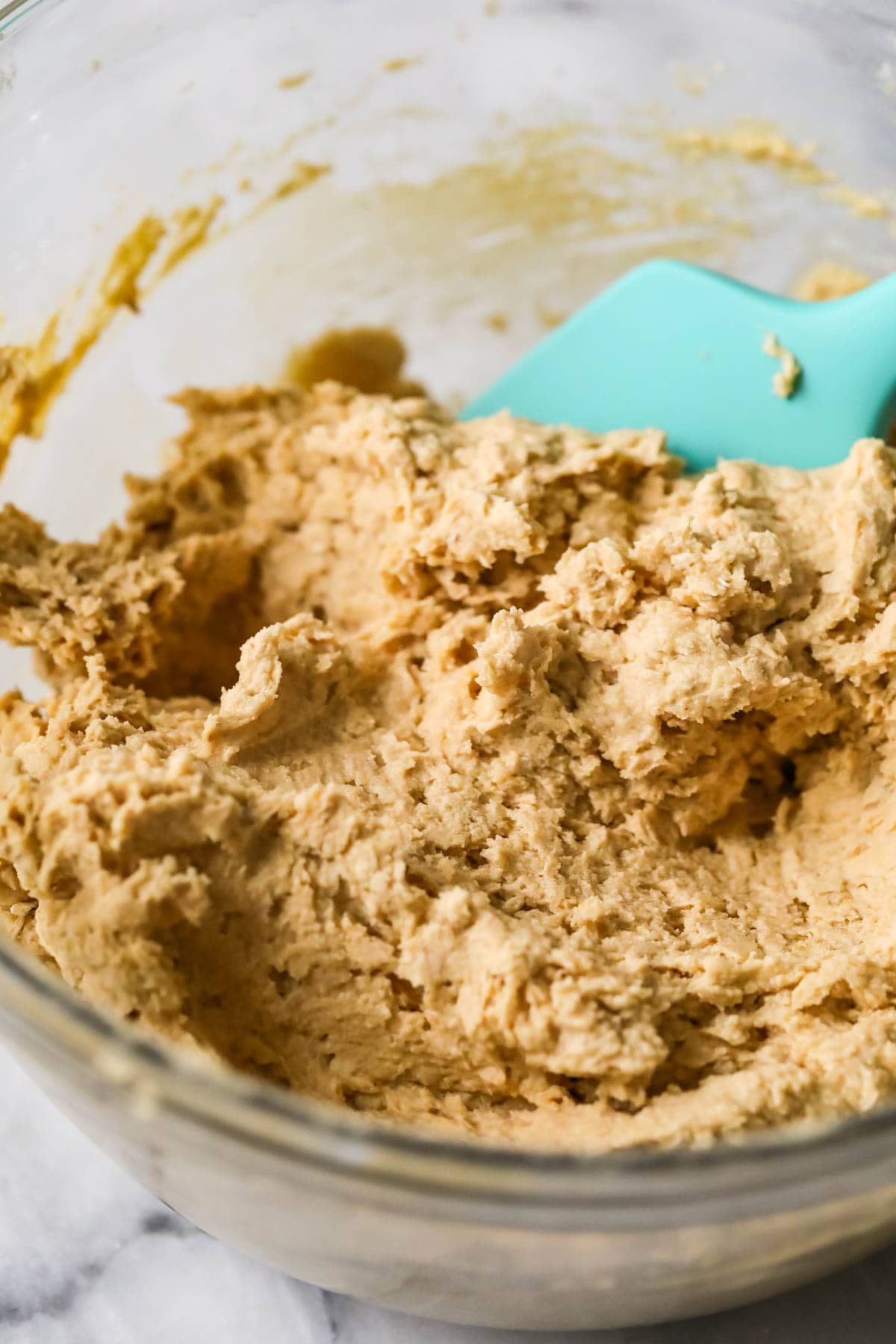 Bowl of cookie dough being mixed together with a bright blue spatula.