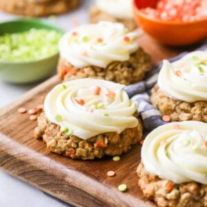 Carrot cake cookies toped with cream cheese frosting and sprinkles on a wood cutting board.