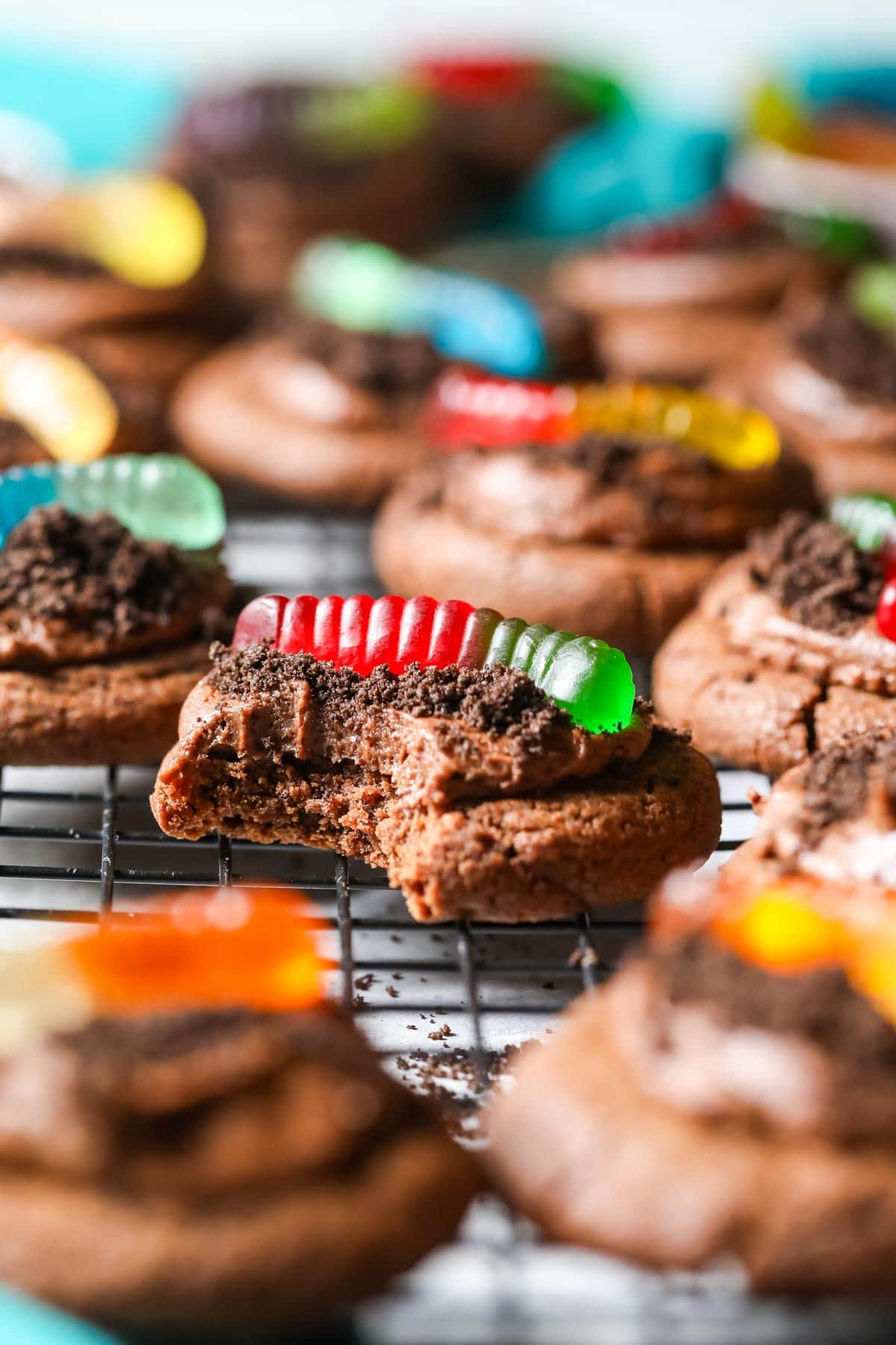 Bite missing from a chocolate cookie topped with Oreo crumbs and gummy worms.