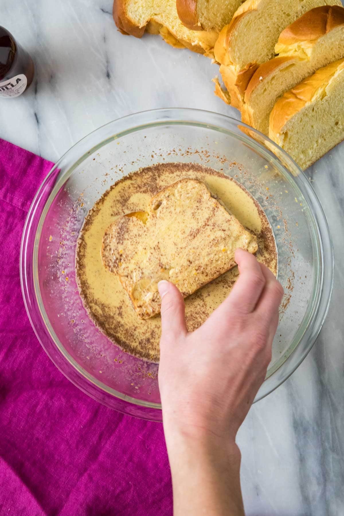 Overhead view of a slice of brioche bread being dipped into a custard mixture.