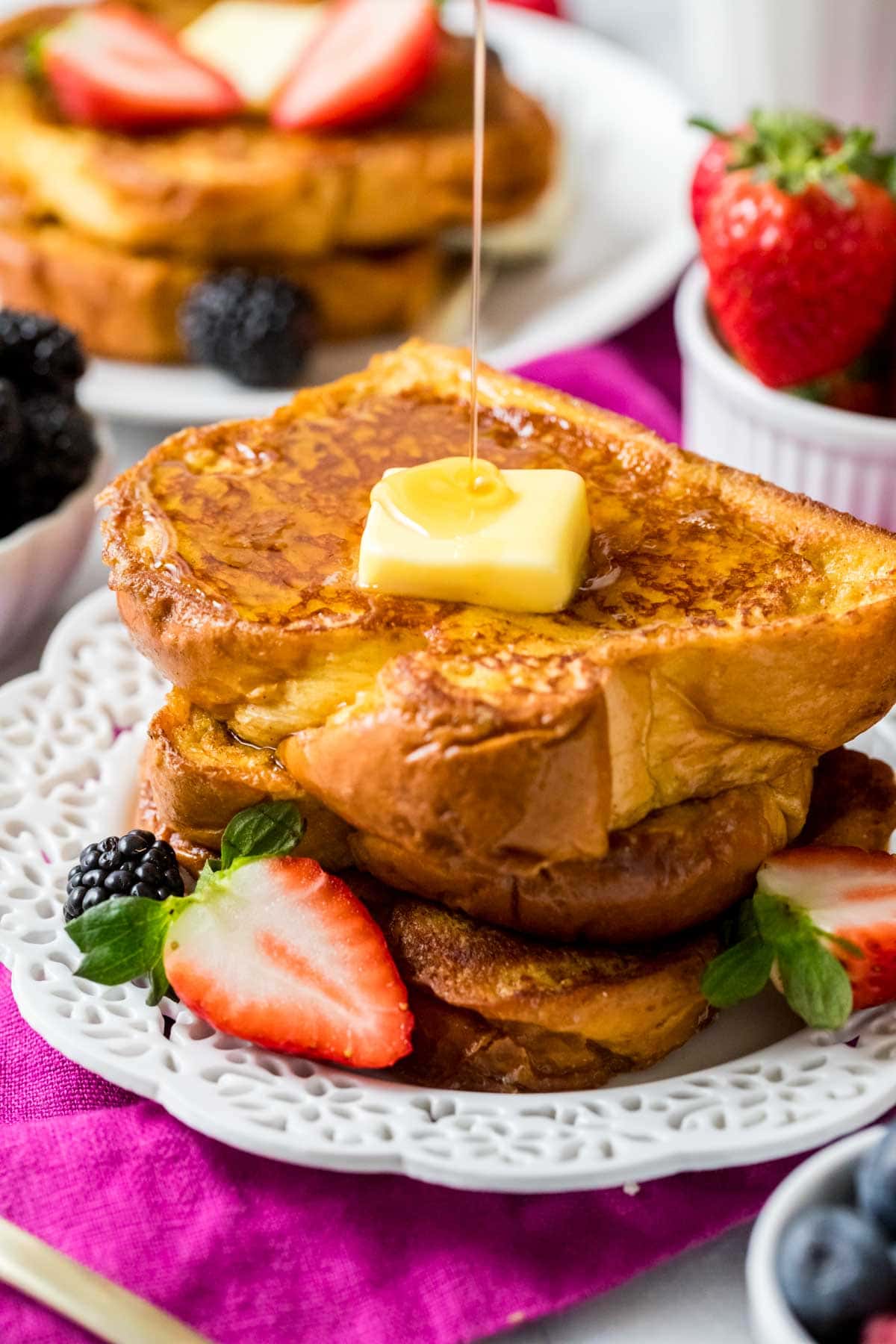 Stack of brioche french toast topped with a pat of butter and a drizzle of maple syrup.