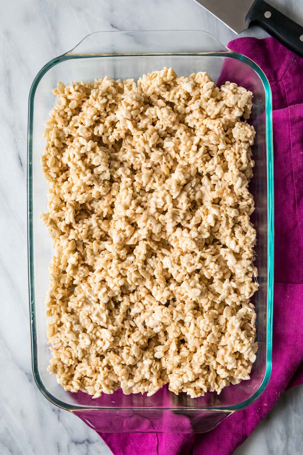 Overhead view of a rice krispies cereal mixture that's been gently pressed into a 9x13 glass pan.