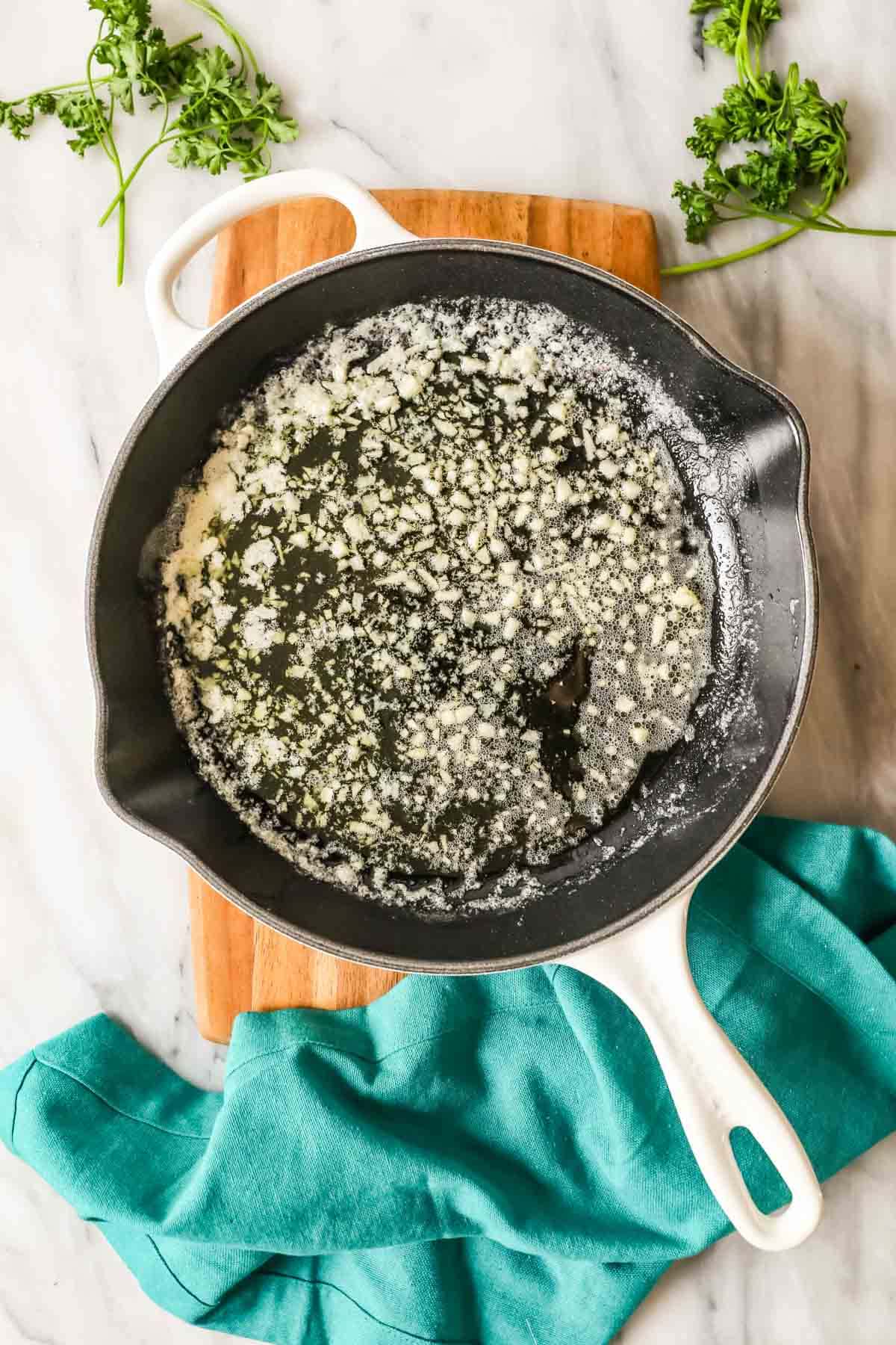 Overhead view of garlic cooking in a pan of butter.