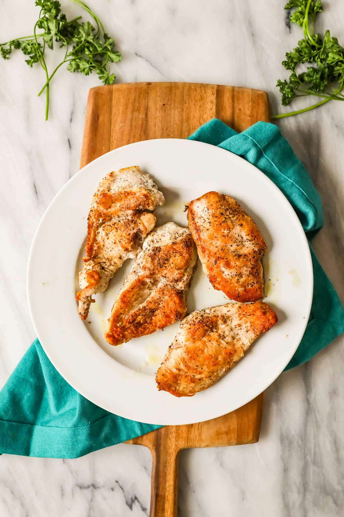 Overhead view of seared chicken breasts on a white plate.