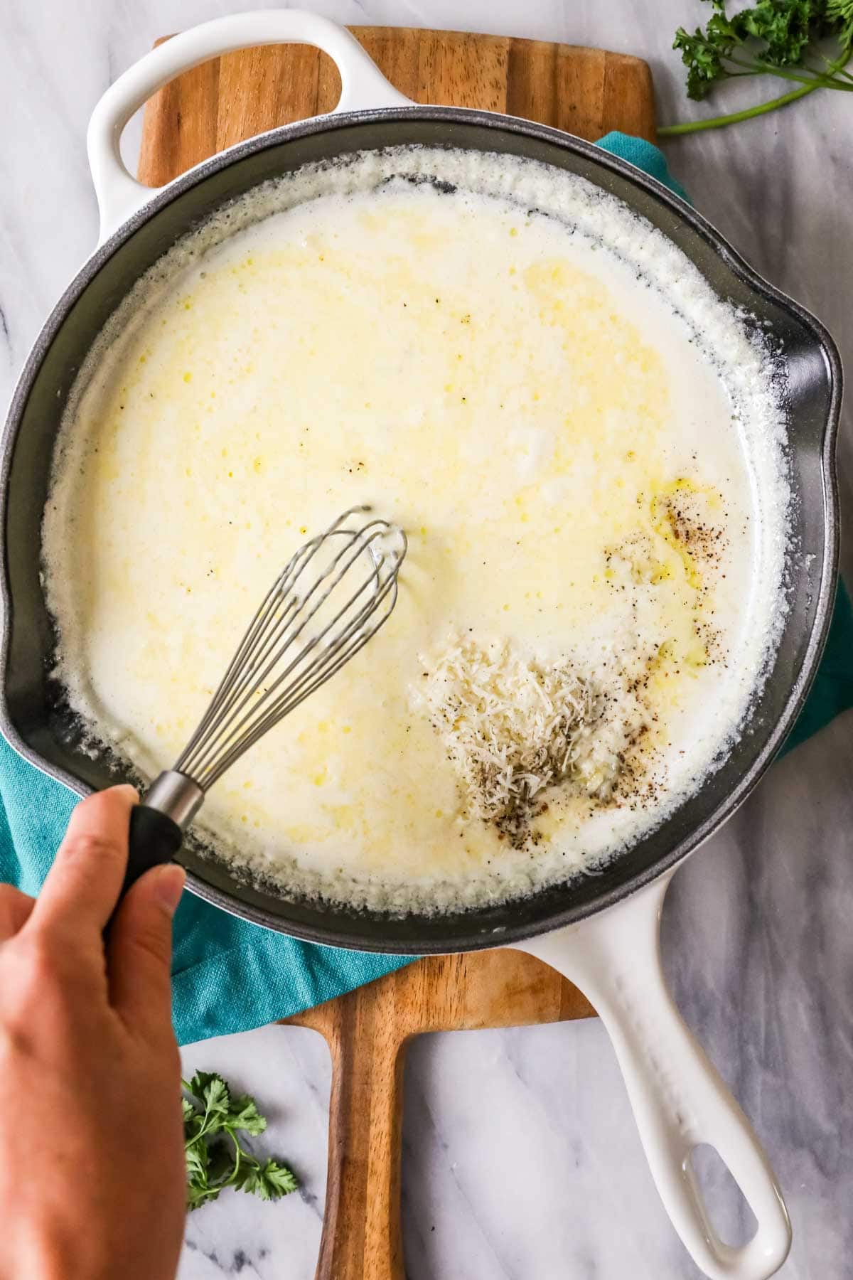 Overhead view of parmesan cheese being whisked into alfredo sauce.