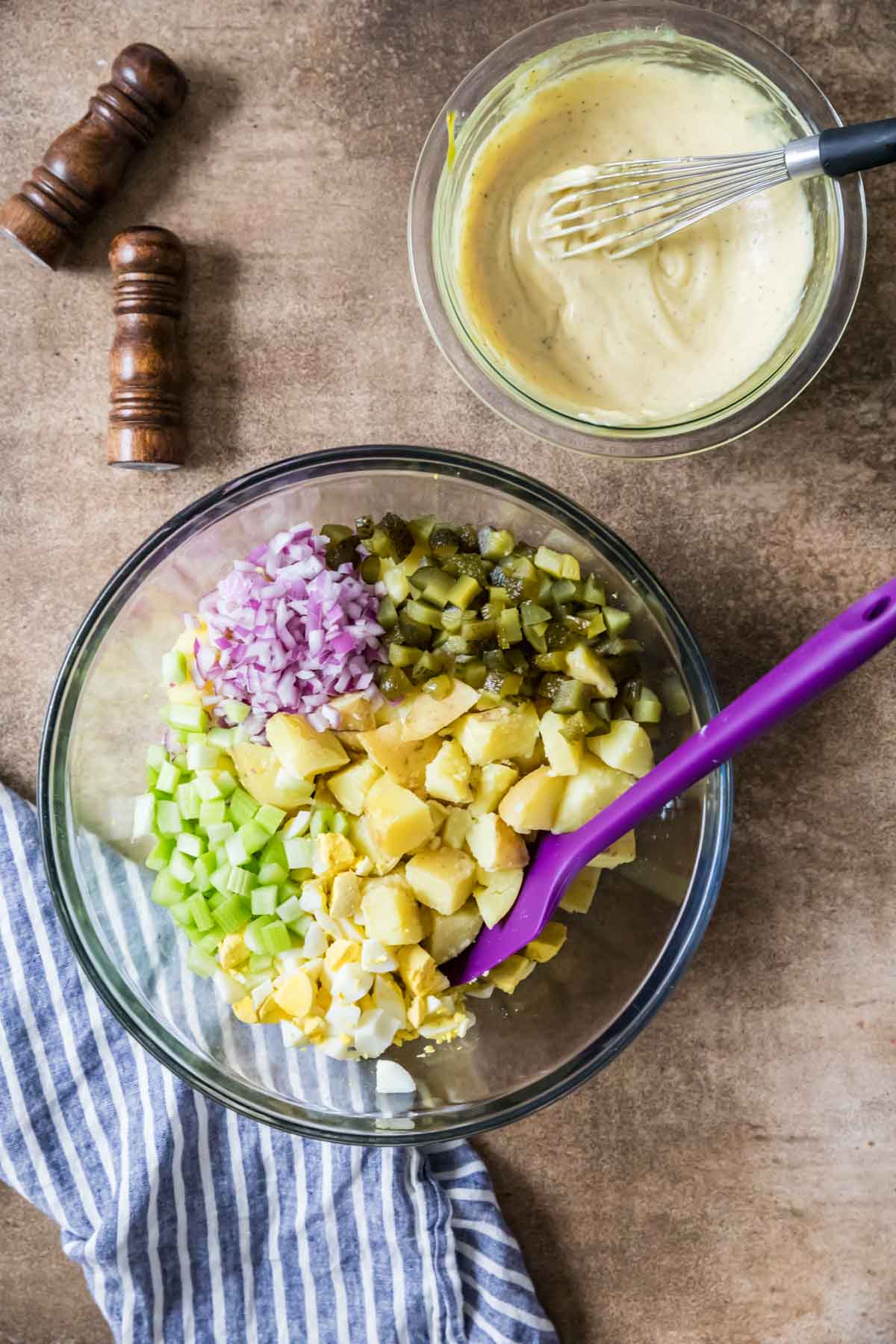 Overhead view of a bowl of potato salad components with the dressing sitting beside it.