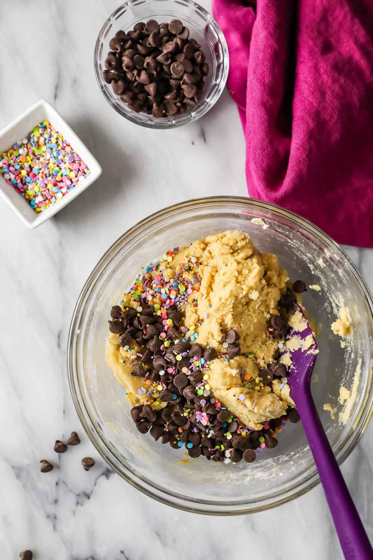 Overhead view of cookie dough in a bowl with chocolate chips and sprinkles on top before mixing in.