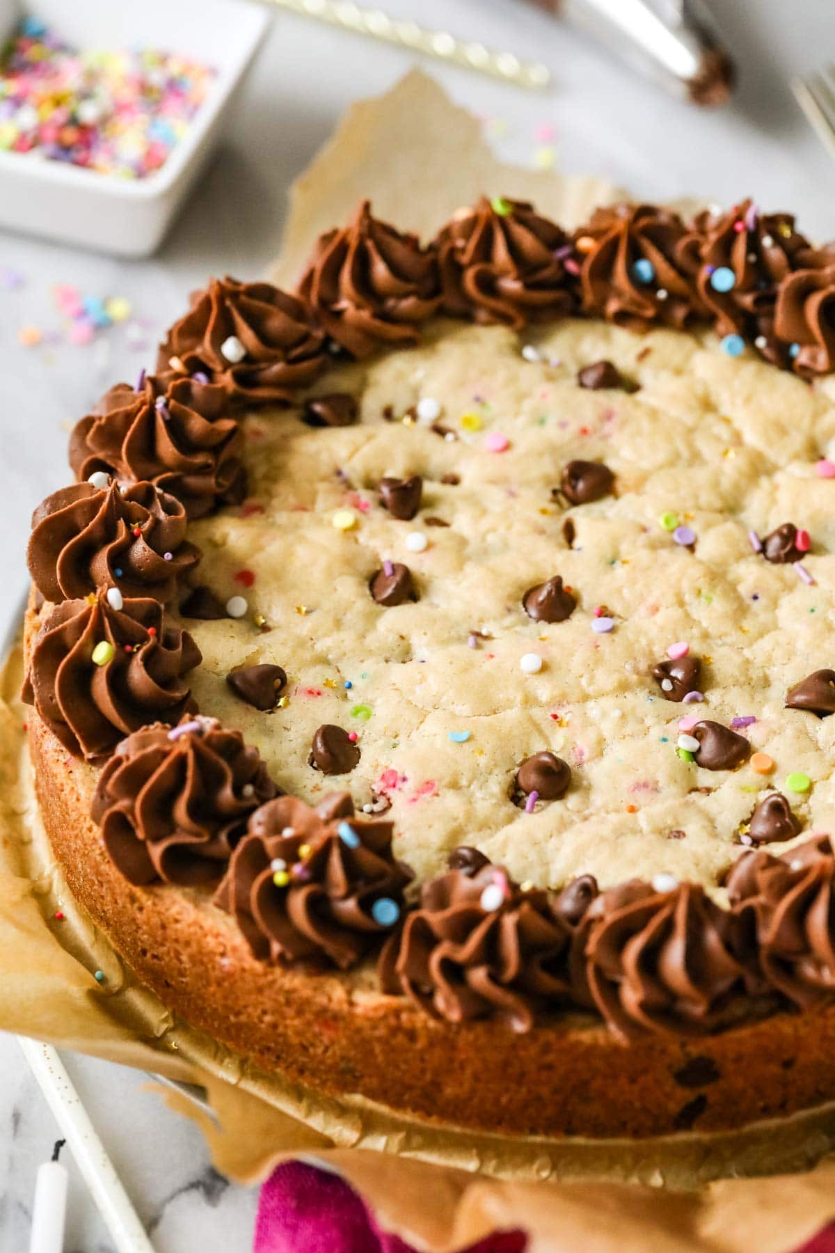 Close-up view of a chocolate chip cookie cake topped with a ring of chocolate frosting and sprinkles.