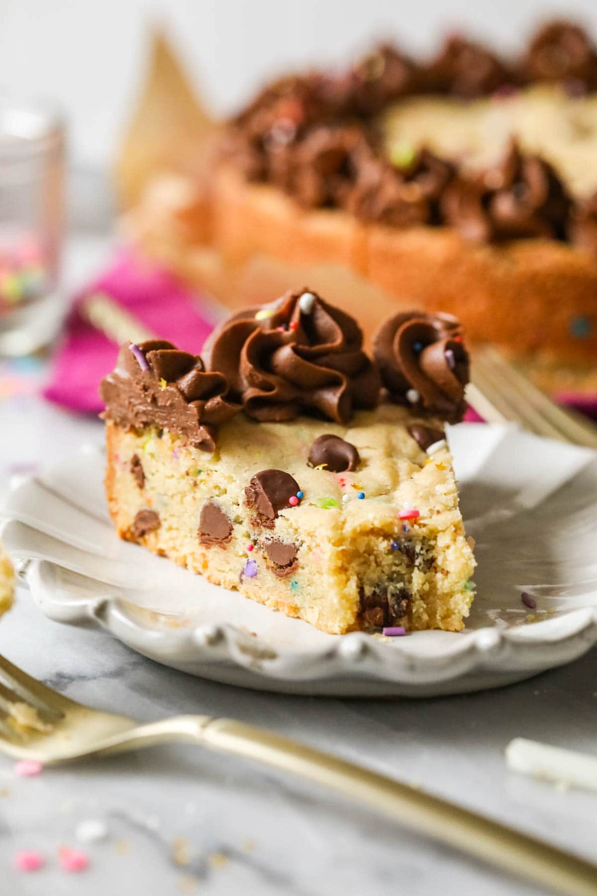 Slice of chocolate chip cookie cake on a plate with one bite missing.