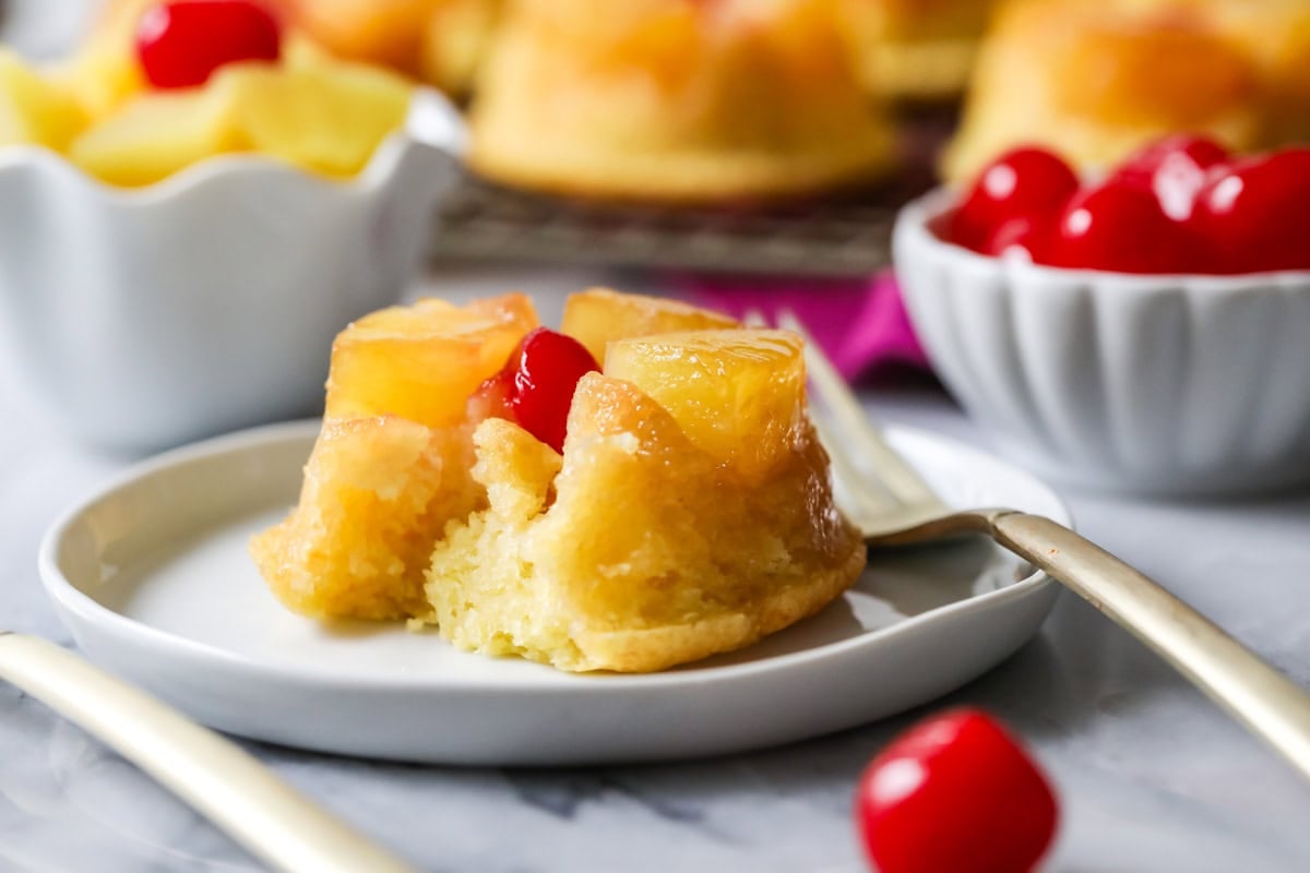 Bite missing from a cupcake topped with pineapple and cherries.