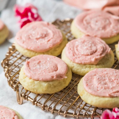 Sour cream cookies topped with a pale pink frosting on a cooling rack.