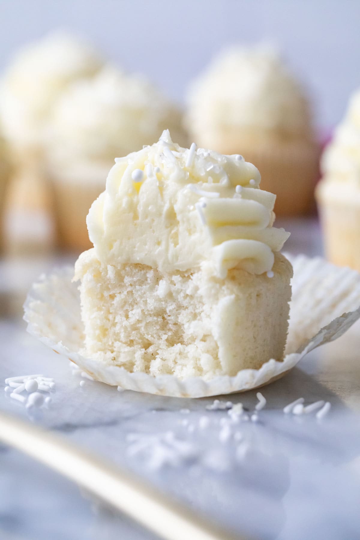 White cupcake sitting in its wrapper with one bite missing.