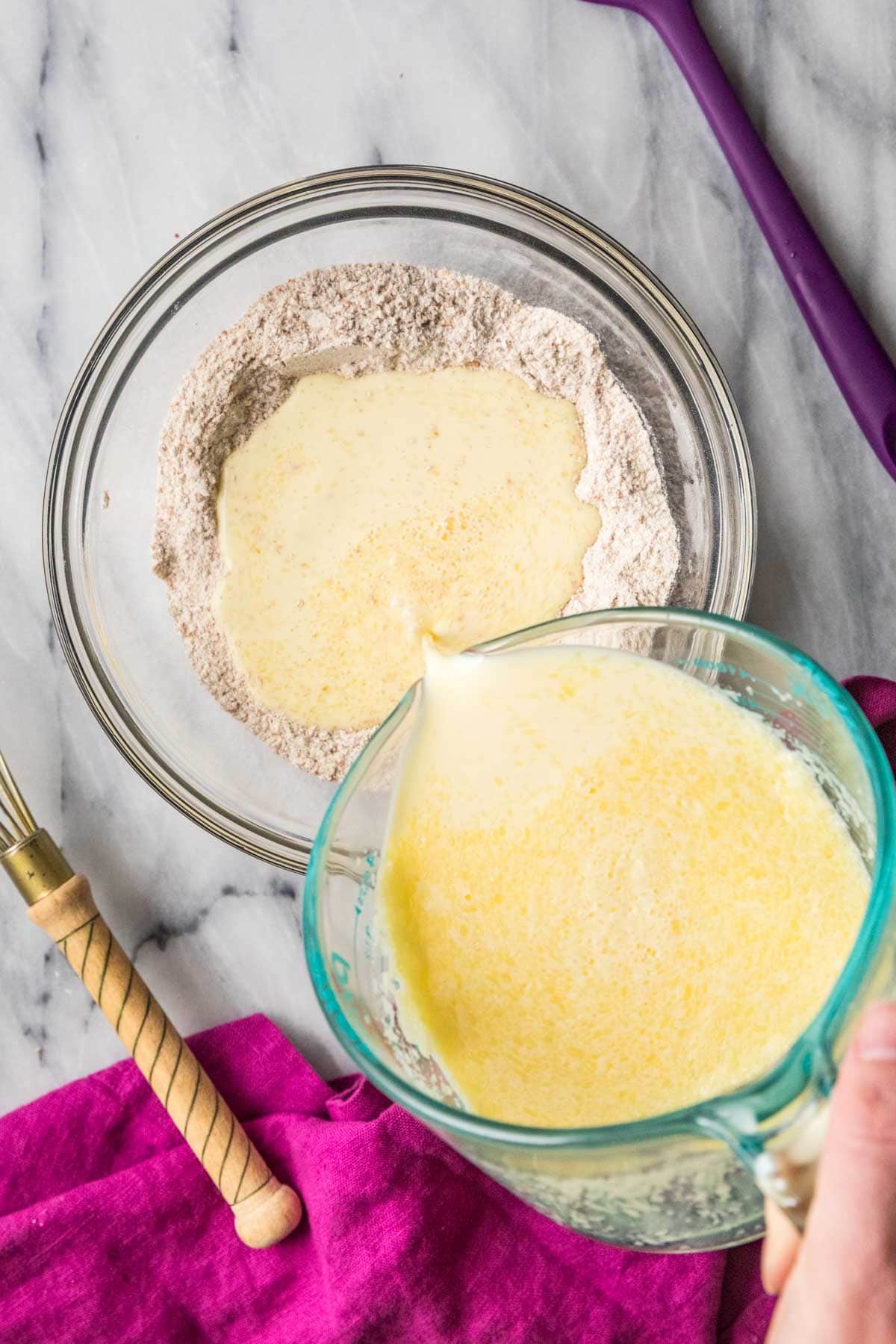 Overhead view of a butter, egg, and milk mixture being poured into dry ingredients.