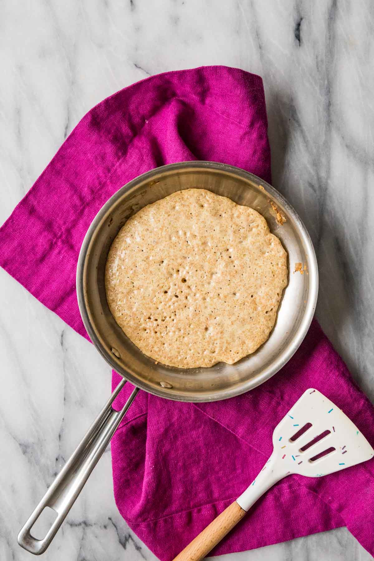 Overhead view of a pancake cooking in a skillet.