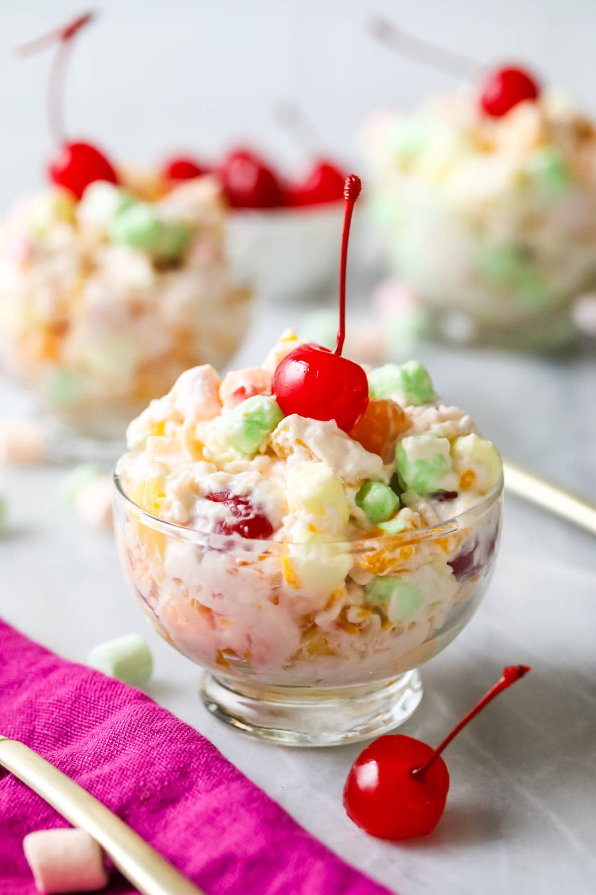 Glass bowl of ambrosia salad topped with a maraschino cherry.