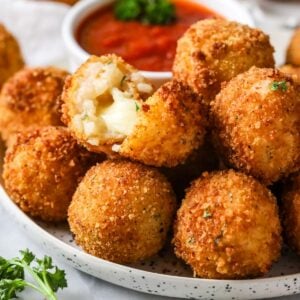 Plate of arancini with one cut in half to show a cheesy filling.