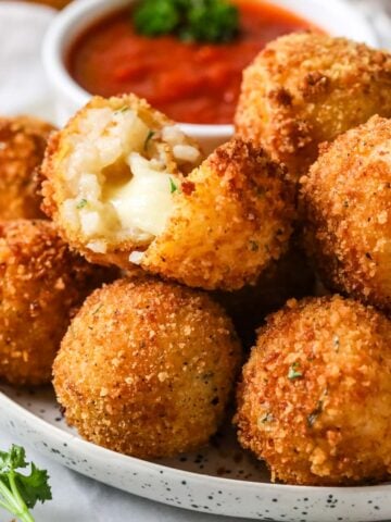 Plate of arancini with one cut in half to show a cheesy filling.