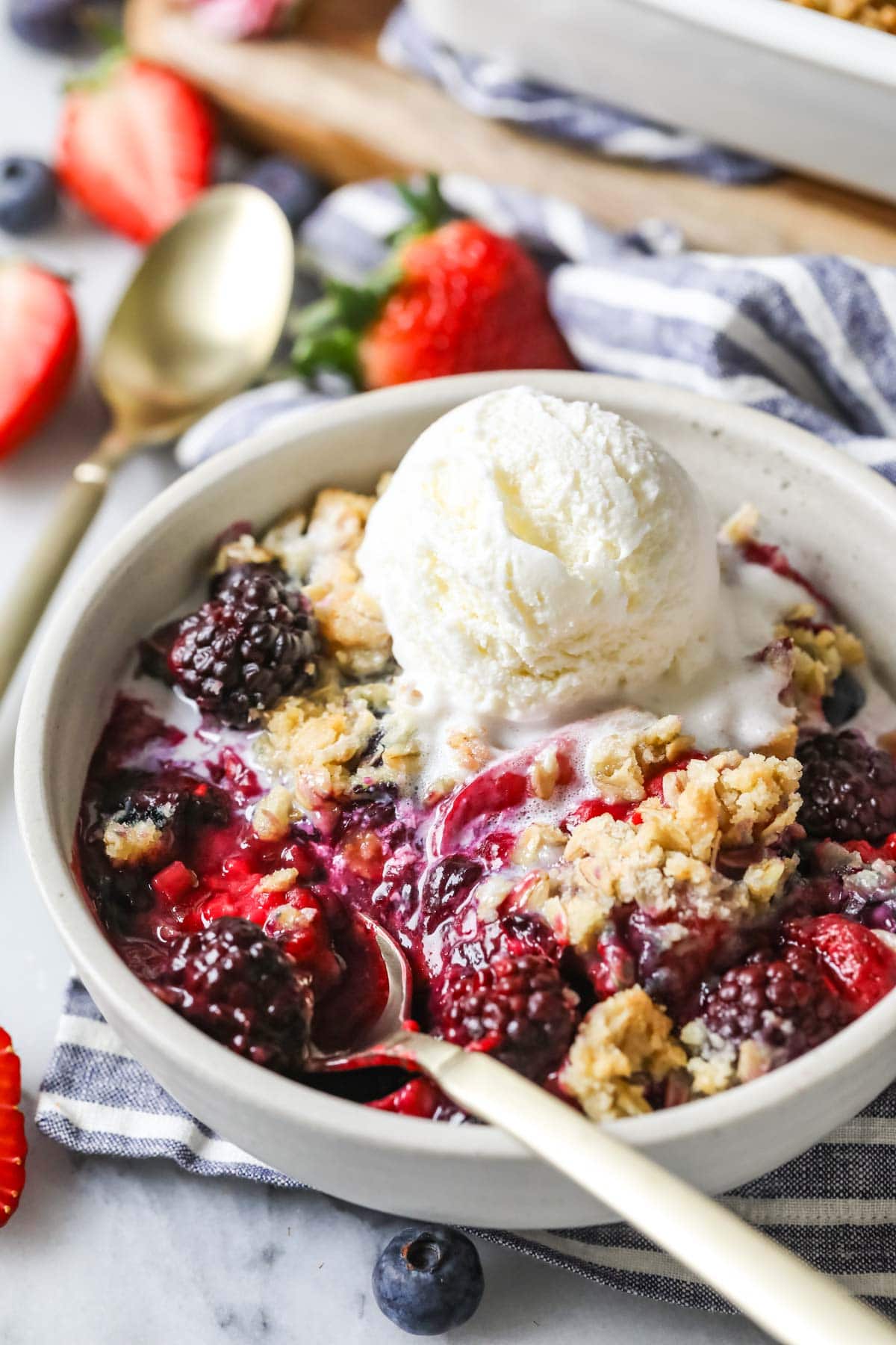 Bowl of berry crisp topped with a melting scoop of vanilla ice cream.