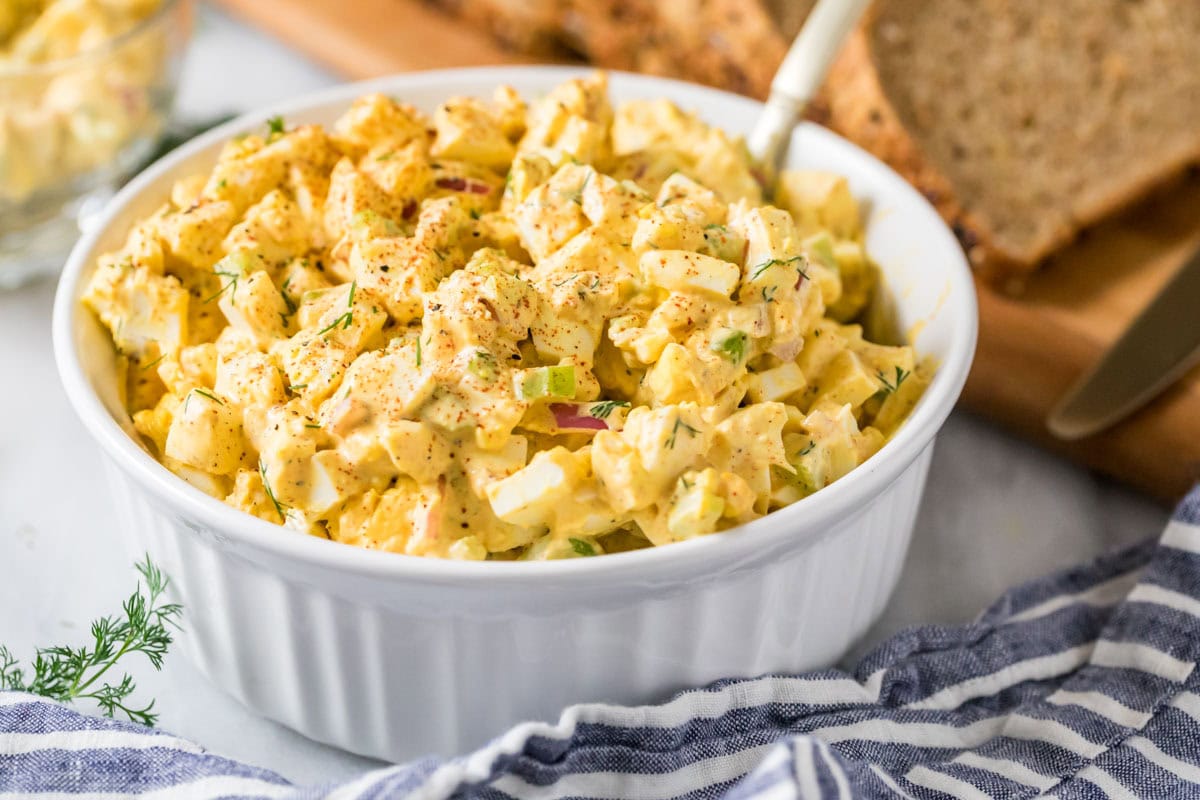 White serving bowl with a salad made from eggs, celery, onions, and more.