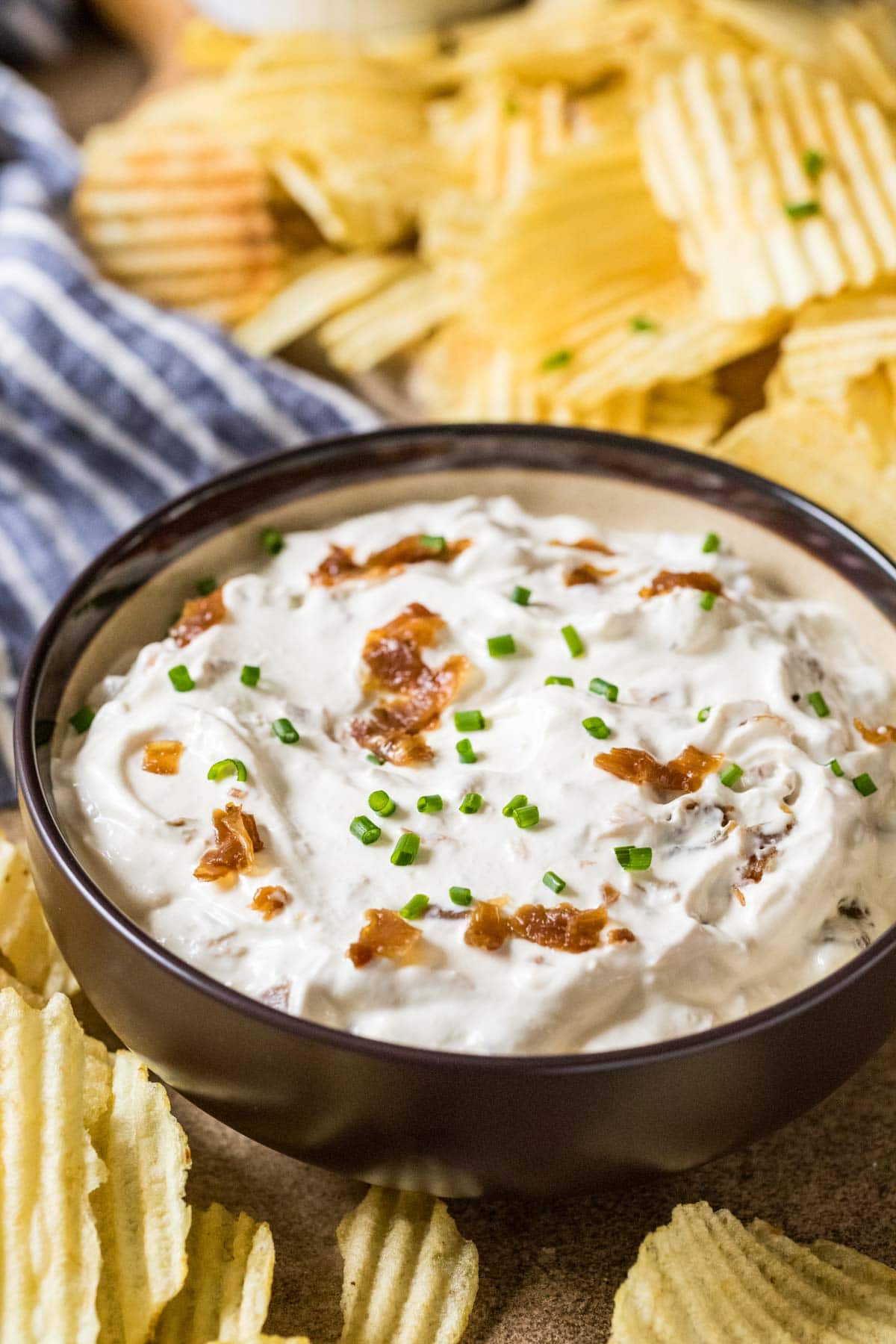 Bowl of dip made with sour cream, caramelized onions, and chives surrounded by ripple potato chips.