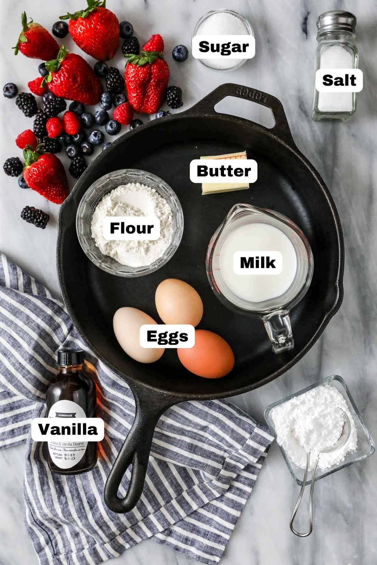 Overhead view of labelled ingredients in a cast iron pan including flour, eggs, powdered sugar, and more.