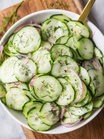 Overhead view of a serving bowl of cucumber salad made with dill and red onion.