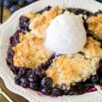 Serving of blueberry cobbler topped with a scoop of vanilla ice cream in a white dish.