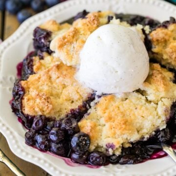 Serving of blueberry cobbler topped with a scoop of vanilla ice cream in a white dish.
