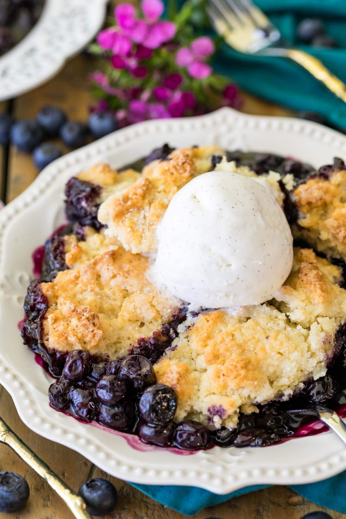 Serving of blueberry cobbler topped with a scoop of vanilla ice cream in a white dish.