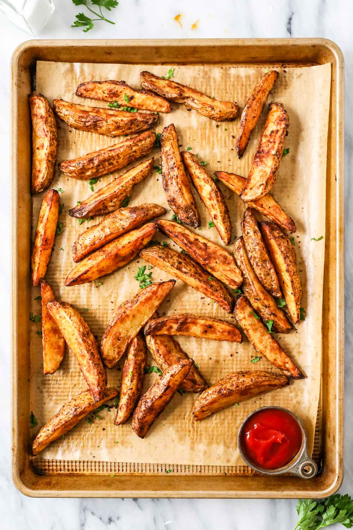 Overhead view of potato wedges on a baking sheet after baking.