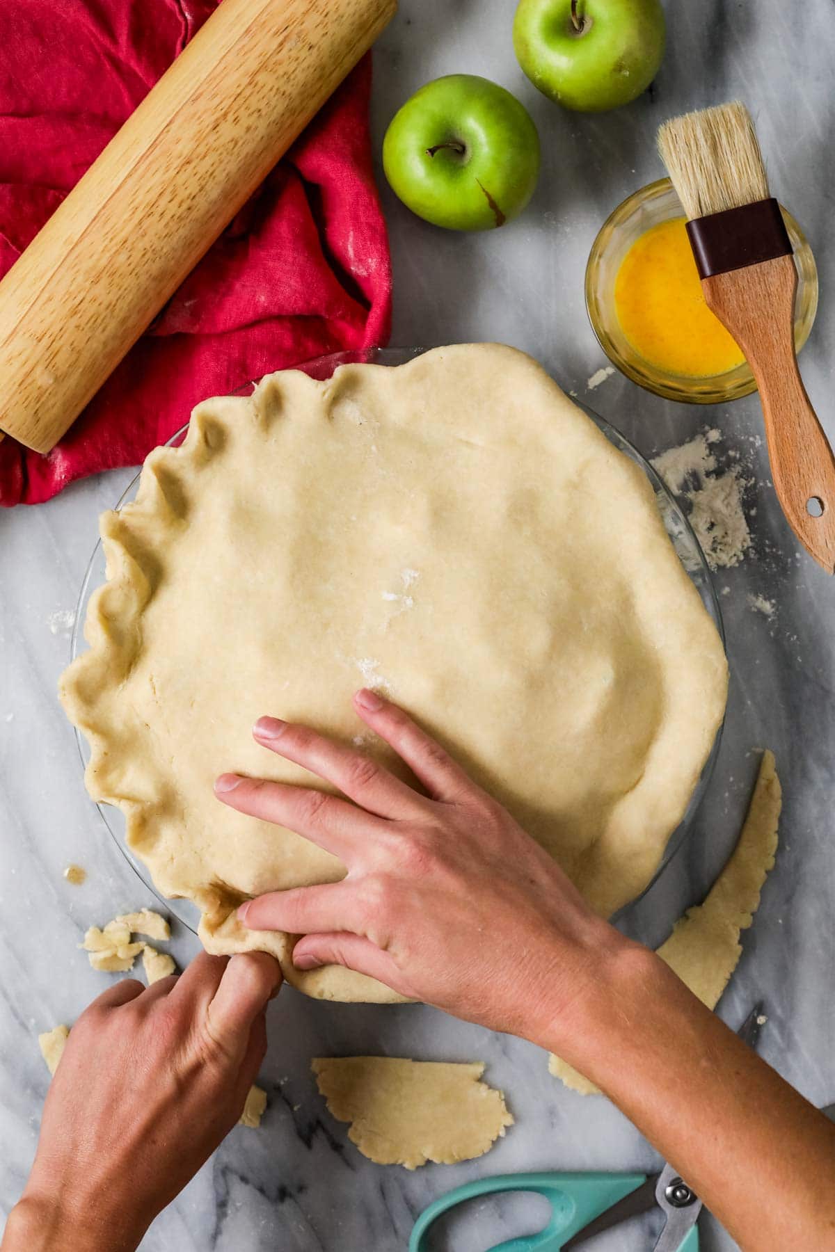Hands pinching a crimped edge on a pie crust.