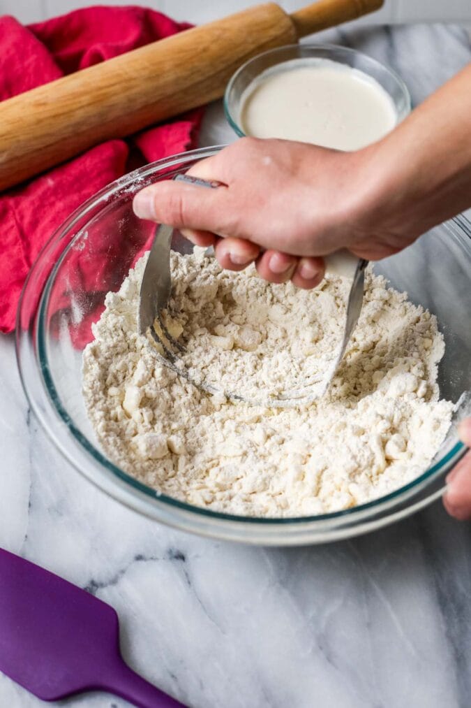 Using a pastry cutter to work butter into a flour mixture for pie sourdough crust.