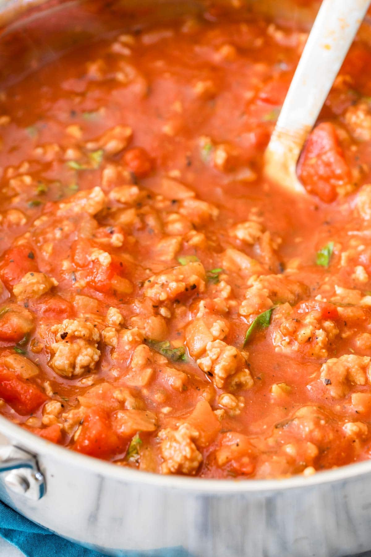 Close-up view of a pot of pasta sauce made with sausage and fresh basil.
