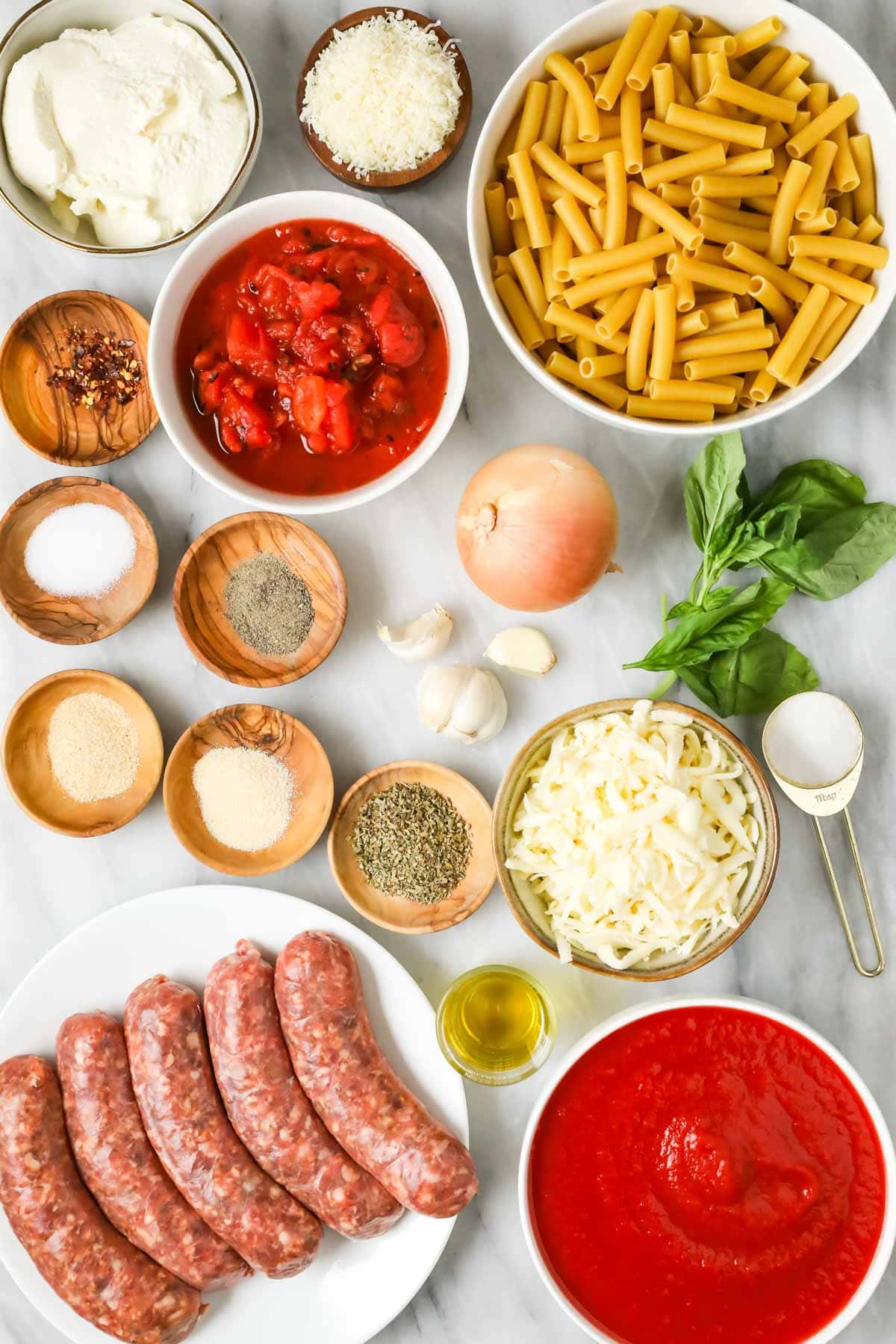 Overhead view of ingredients including sausage, tomato sauce, ziti noodles, and more.