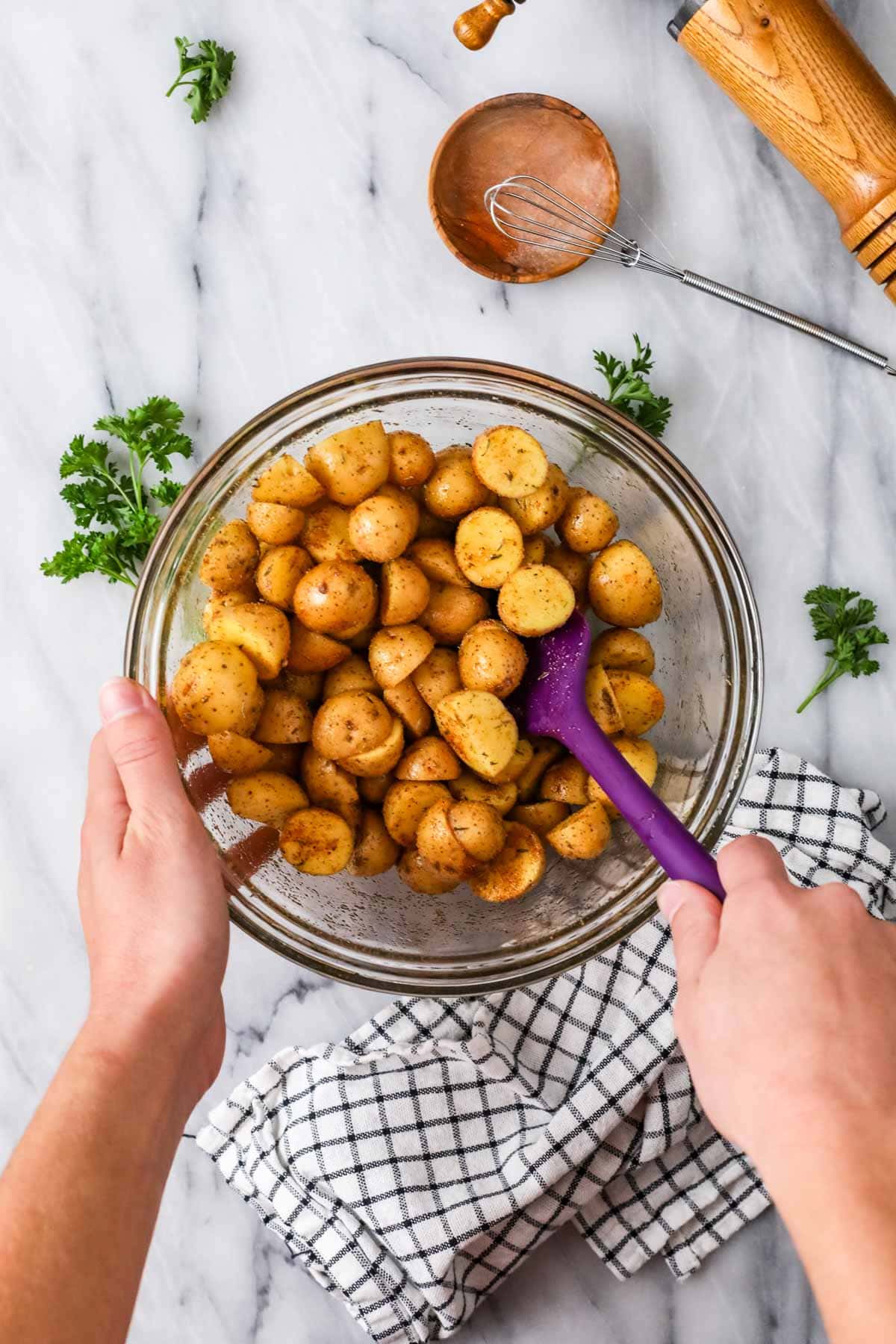 Overhead view of a bowl of small potatoes being tossed in olive oil and spices.