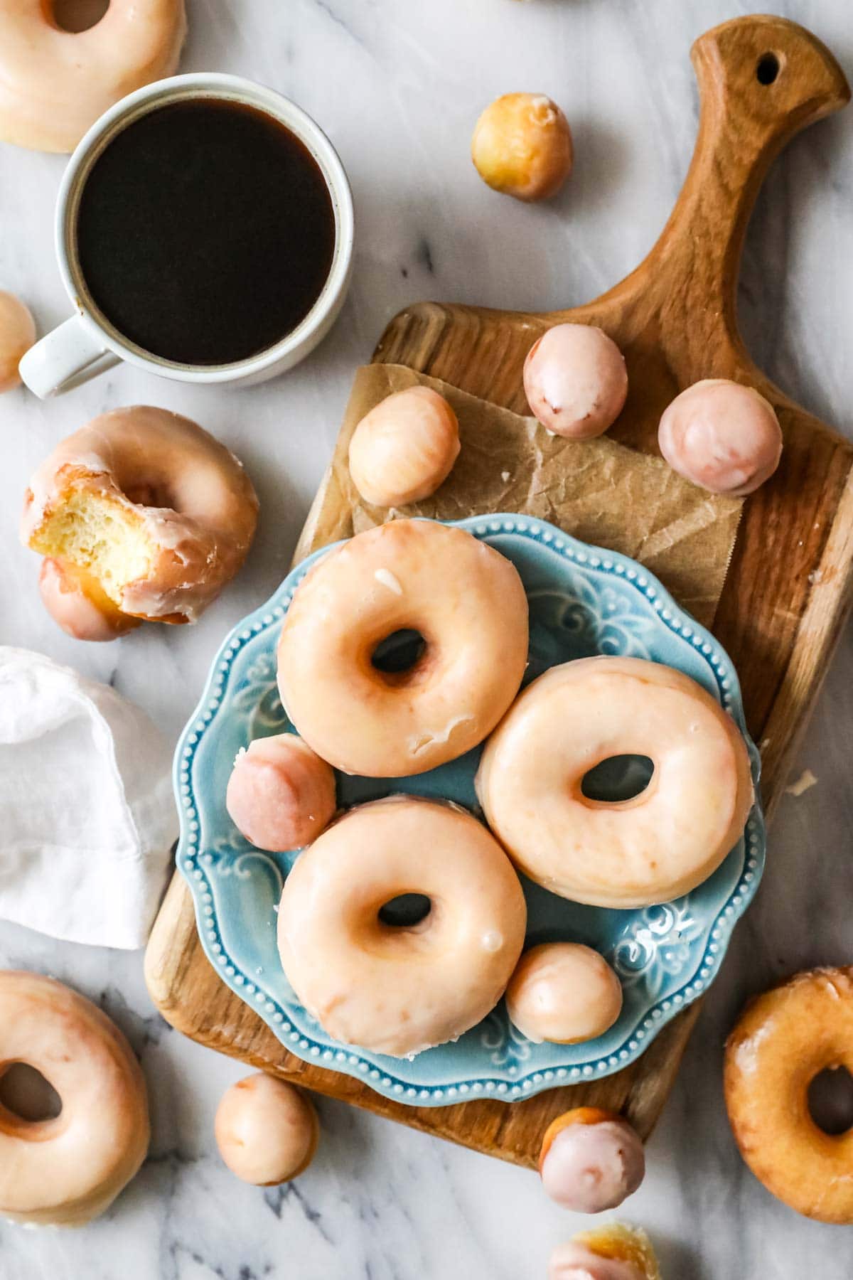 Overhead view of sourdough donuts and donut holes on a plate surrounded by more donuts and a cup of coffee.