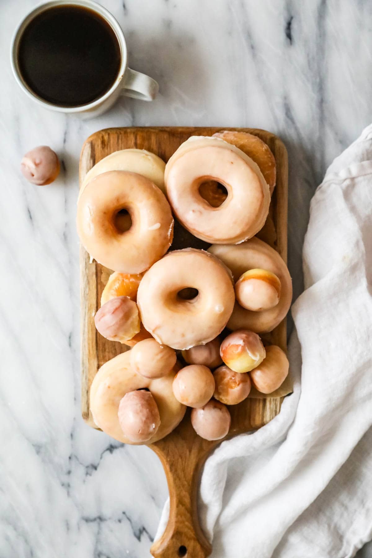 Wooden serving tray with a pile of glazed donuts made with sourdough starter instead of yeast.