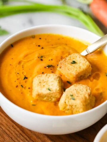 Bowl of roasted carrot soup topped with croutons.
