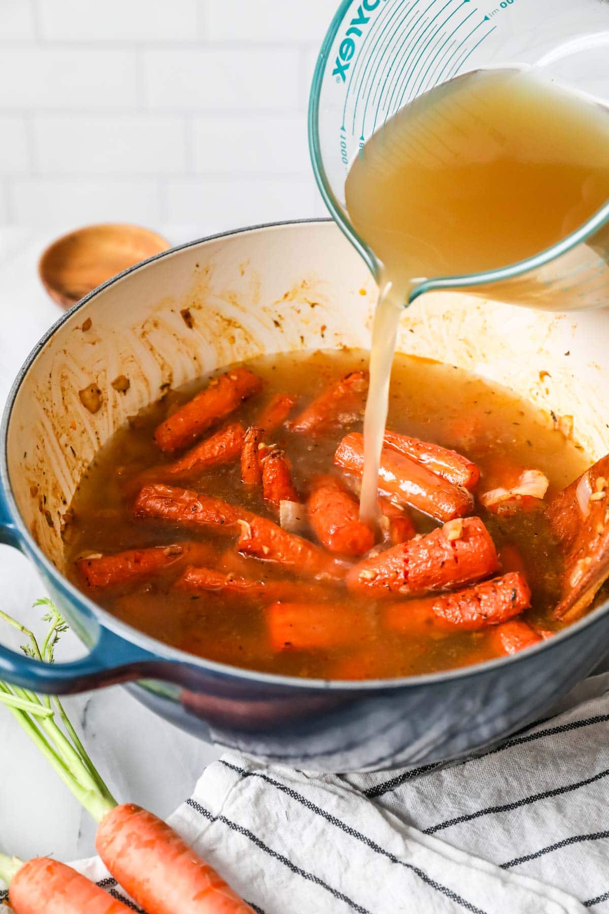 Broth being poured into a dutch oven with roasted carrots and onions inside.