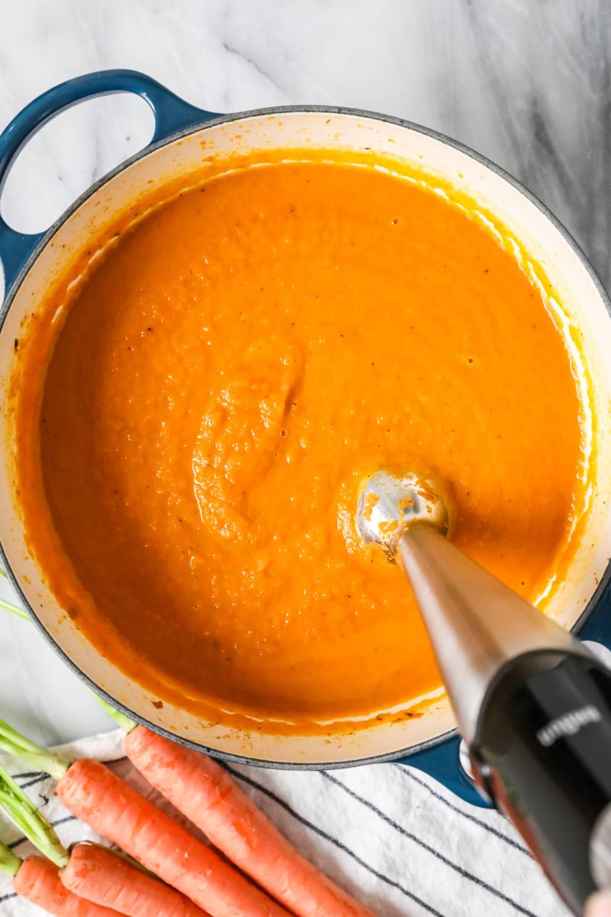 Overhead view of carrot soup being blended with an immersion blender.