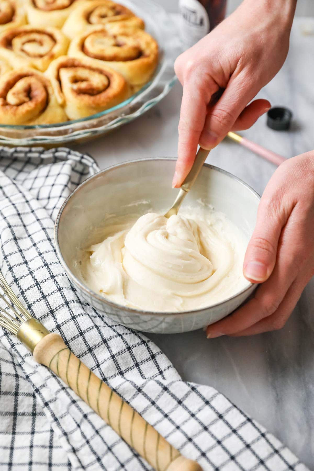 Stirring cinnamon roll icing beside a pan of unfrosted rolls.
